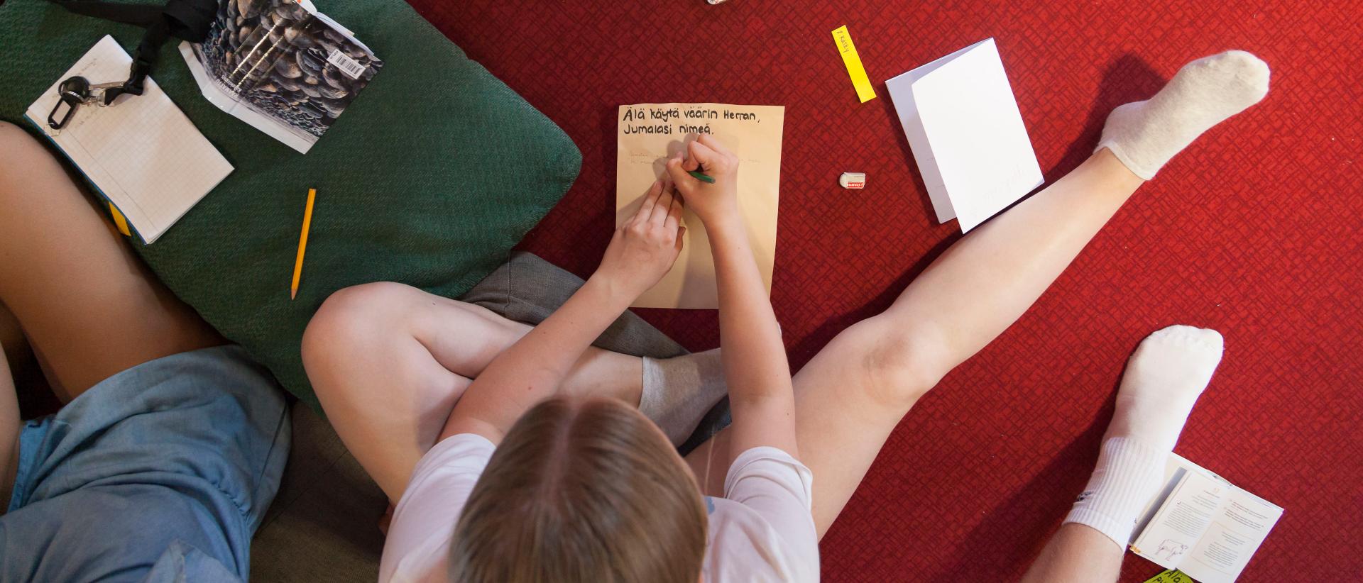 Tyttö kirjoittaa muistiinpanoja Malmin seurakunnan rippileirillä