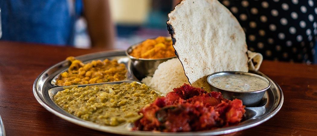 Kuvassa nepalilaista ruokaa metallilautasella, riisiä, kastiketta ja kasviksia sekä #rohkeastiyhdessä -teksti
