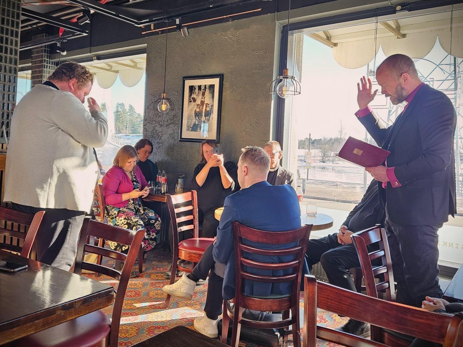 Ihmisiä istumassa, piispa rukoilee