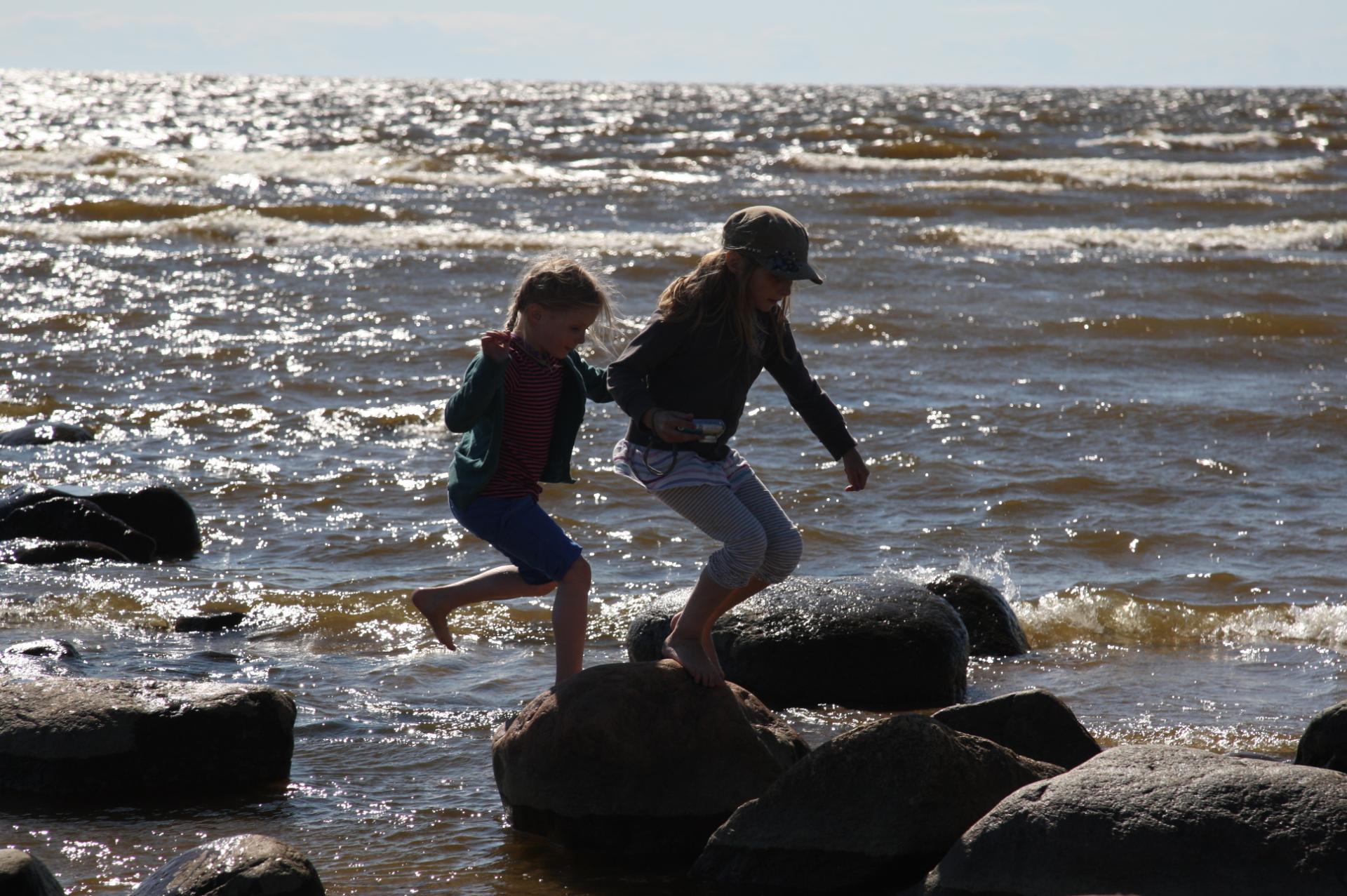 kaksi tyttöä juoksee meren rantakivillä