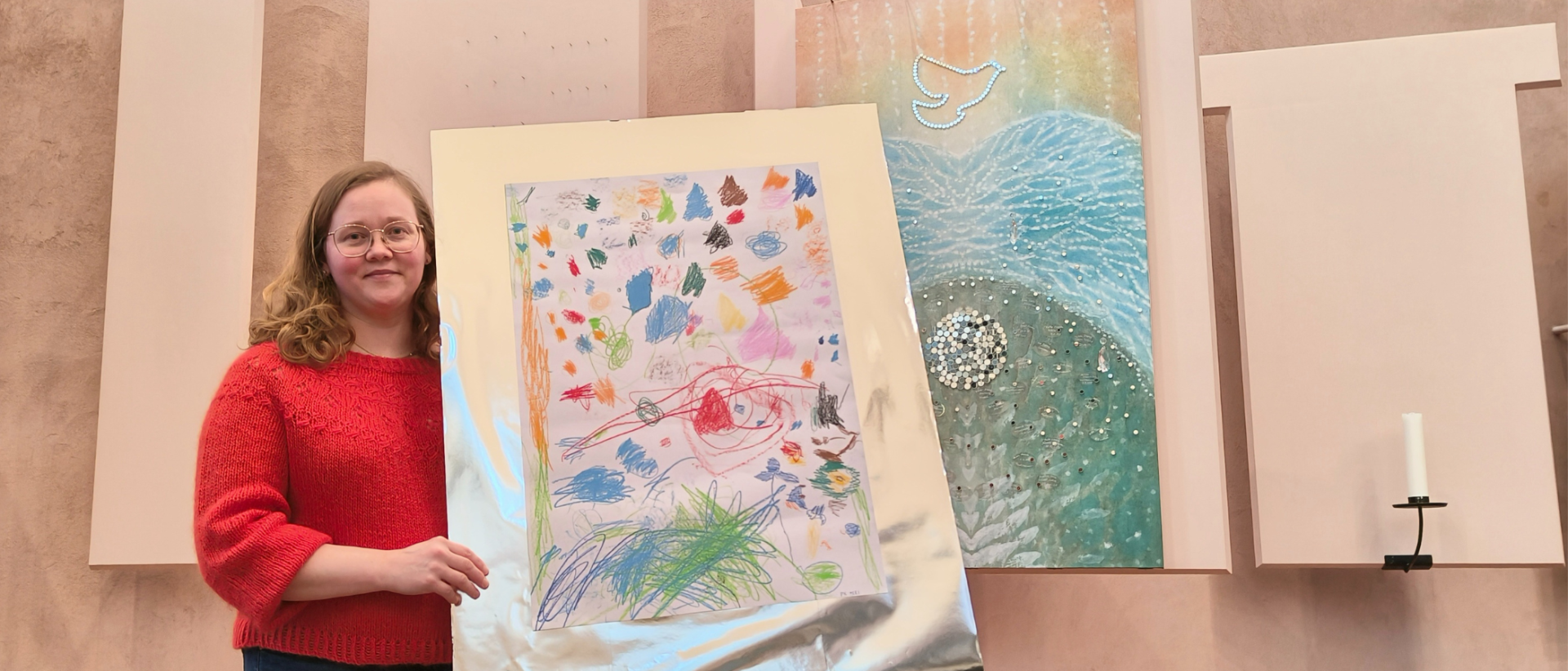 Susanna Stendahl lasten tekemän Kirkkokuvista-työn kanssa Mikaelinkirkon kastepuun edessä