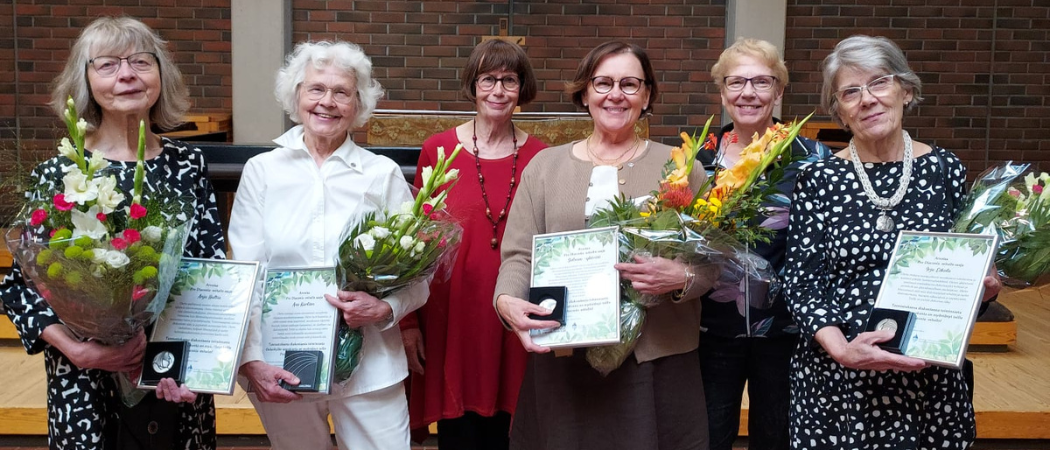 Kuusi naista Oulunkylän kirkolla kädessään kukat ja kunniakirjat.