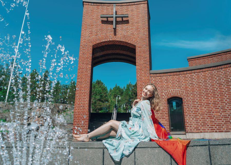 Kuvassa näyttelijä Lenita Susi kuvattuna Leppävaaran kirkolla ja hänellä on sateenkaarilippu. Kuva: Aada Harju