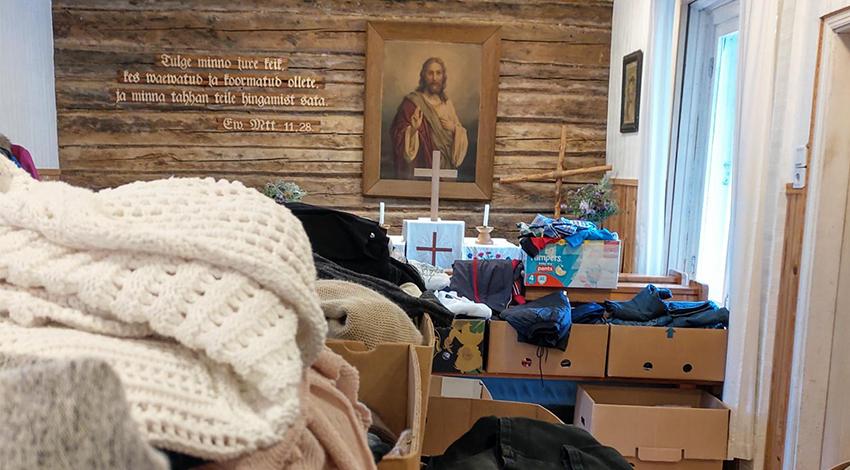 Kirpputori Sakun omakotitalossa toimineen kirkon sisällä. Etualalla kirppistavaraa, takana hirsiseinällä Jeesuksen kuva ja raamatunlause viroksi.