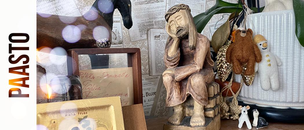 Pianon päällä erilaisia koriste-esineitä ja ikoni, mutta kuvan keskiössä on puusta tehty patsas joka esittää mietteliästä Jeesusta.