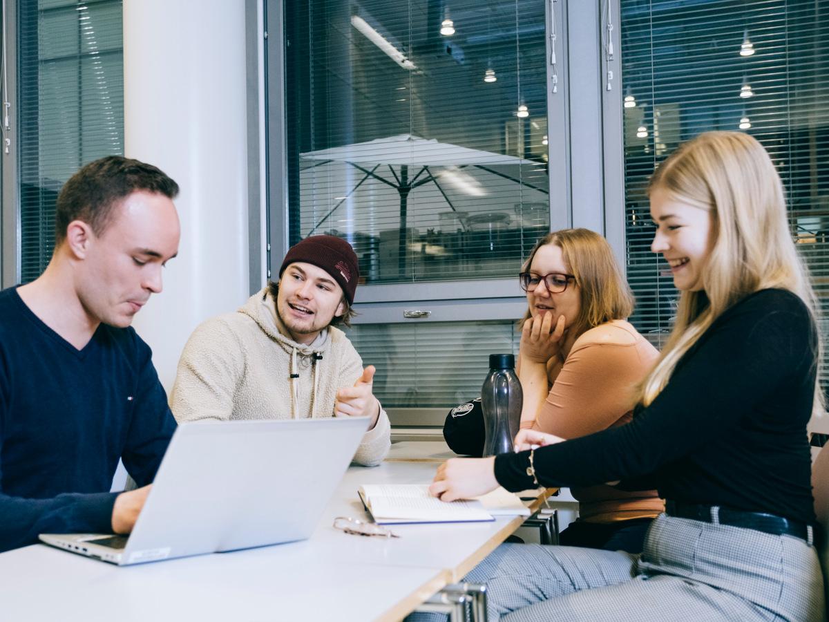 Nuoria opiskelijoita kokoontuneena pöydän ääreen tietokoneen kera