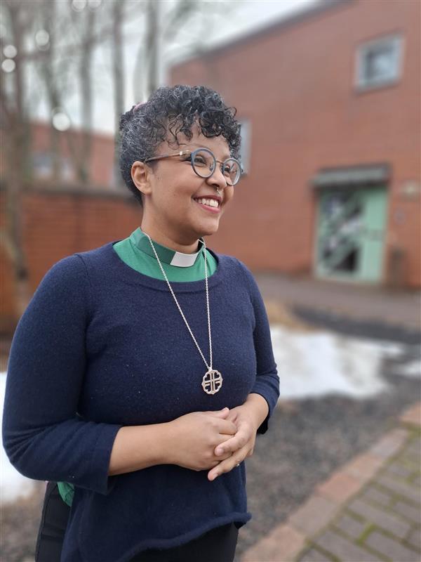 Silmälasipäinen naine seisoo ulkona, taustalla punatiilinen kirkko