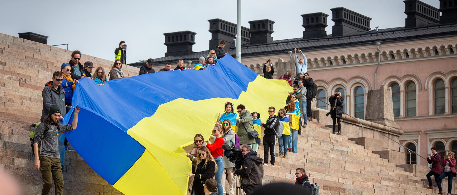 Ihmisiä kantamassa Ukrainan lippua alas Tuomiokirkon portaita. Kuva: Jouni Nieminen