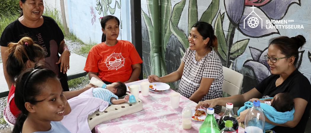 Thaimaan Armonkodin äitejä ja vauvoja ulkona pöydän ääressä.