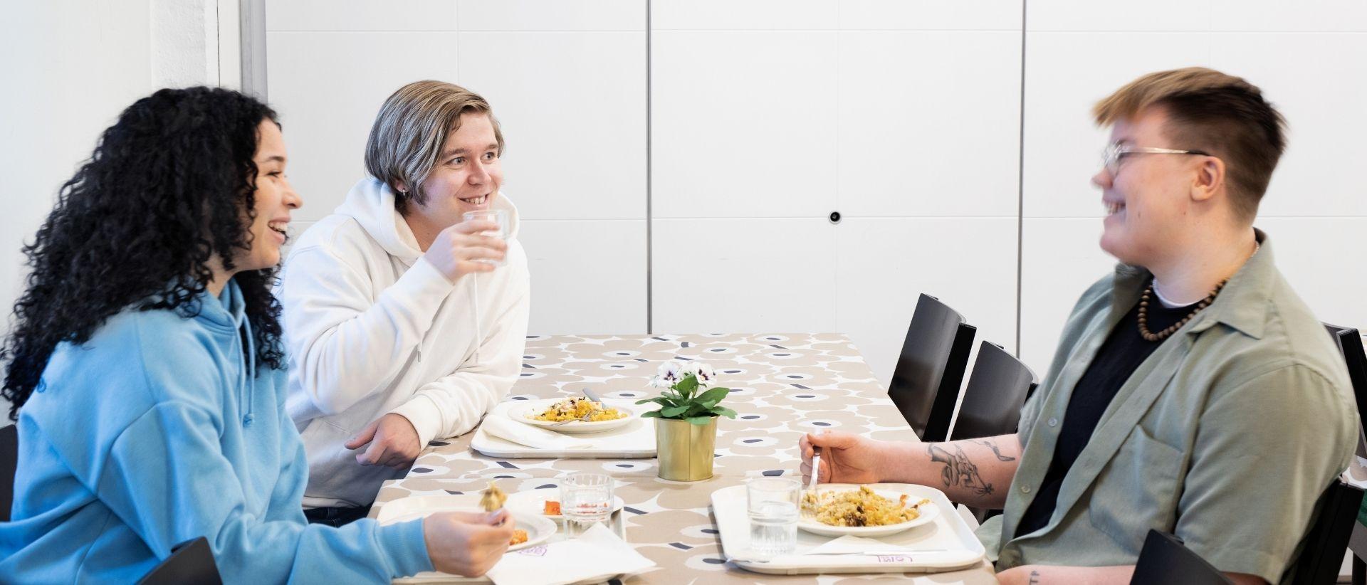 Tre vuxna som sitter runt ett matbord och diskuterar.