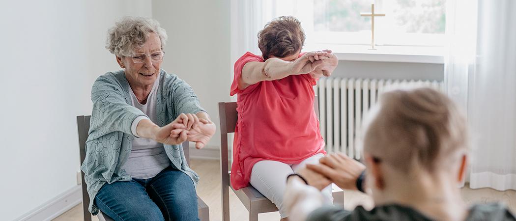 Tuolijumpassa kaksi iloista ikäihmistä ja ohjaaja.