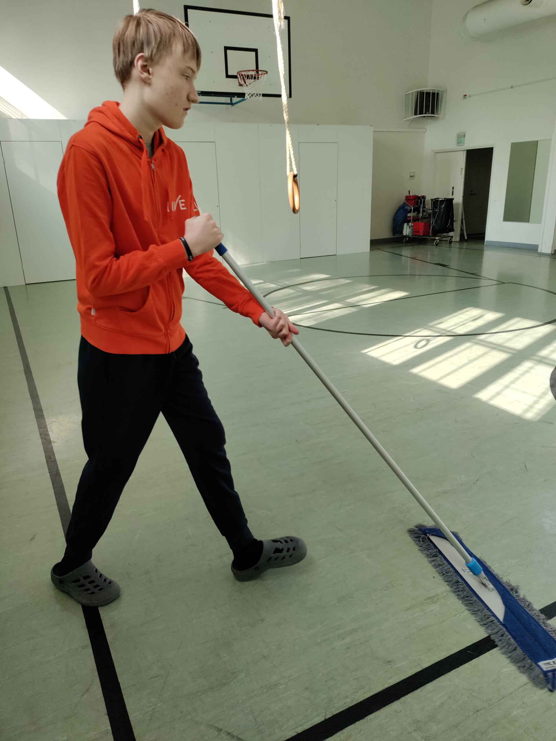 TELMA-opiskelija Olavi Aalto moppaa Vartiokylän kirkon jumppasalin lattiaa