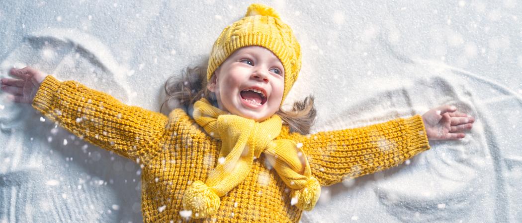 Iloinen lapsi keltaisissa vaatteissa tekee lumienkeli&auml;.