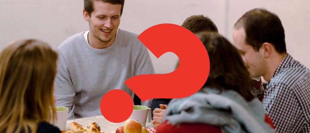 Ihmisiä kokoontuneena yhteisen pöydän ääreen, leppoisa tunnelma. Kuvan päällä punainen kysymysmerkki, joka on Alfa kurssin tunnus.