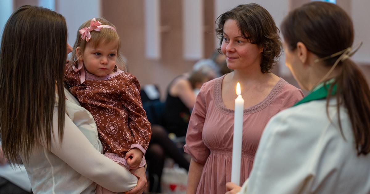 Seurue kastekynttilän äärellä Mikaelinkirkossa. Sylissä olevalla pikkutytöllä rusetti ja mekko. Kuva: Heikki Heikurinen