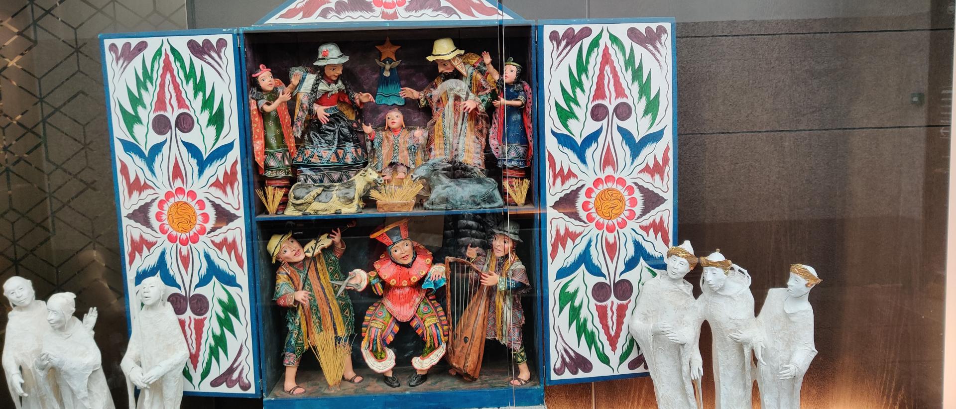 Keskellä kuvaa värikkäitä eteläamerikkalaisia seimihahmoja ja reunoilla vaaleat keraamiset hahmot