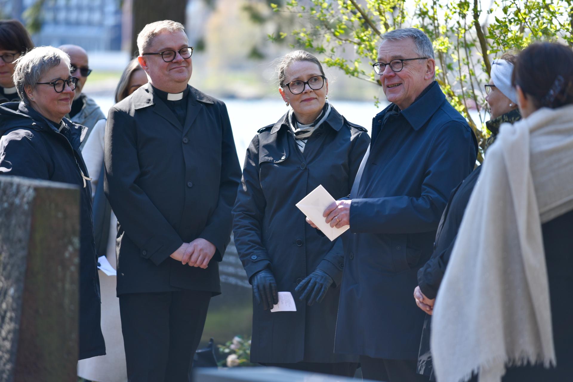 Tummapukuisia ihmisiä seisoo hautausmaalla